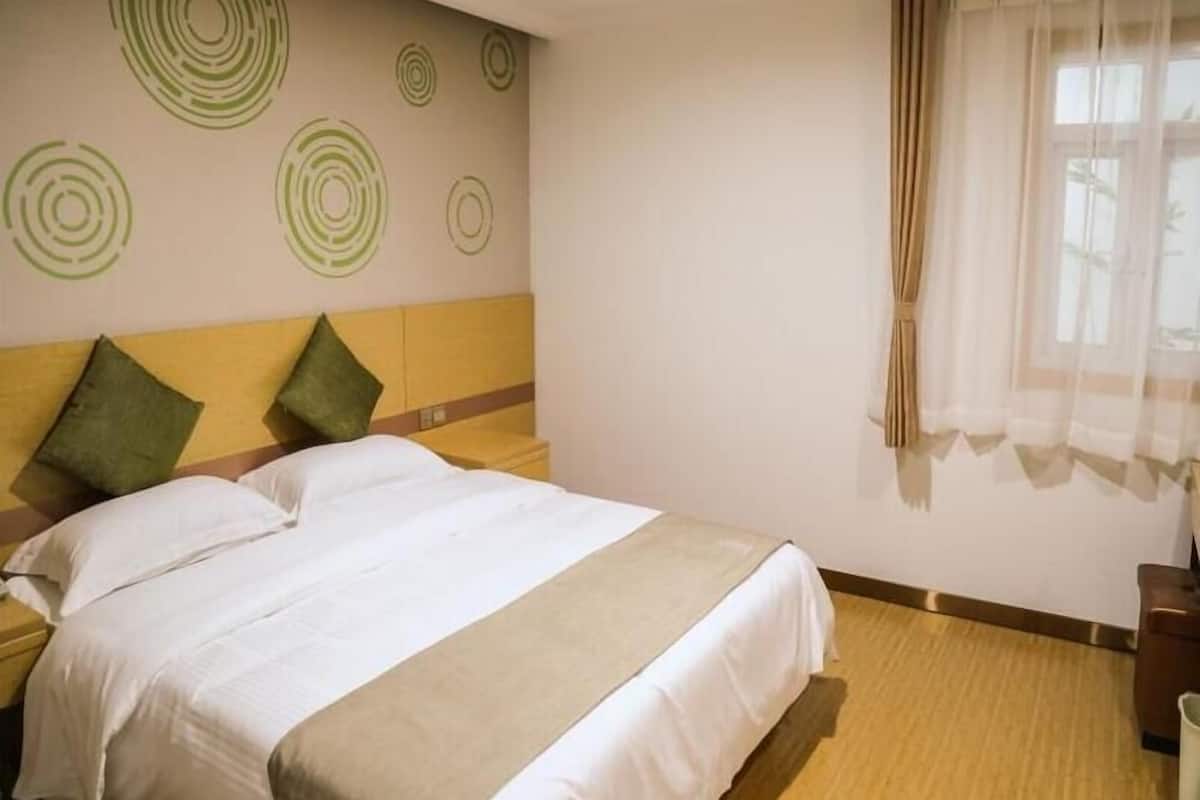 Ein Hotelzimmer mit Bett, zwei Kissen, einem Nachttisch, einer Wand mit kreisförmigen Mustern und einem Fenster mit Vorhängen.