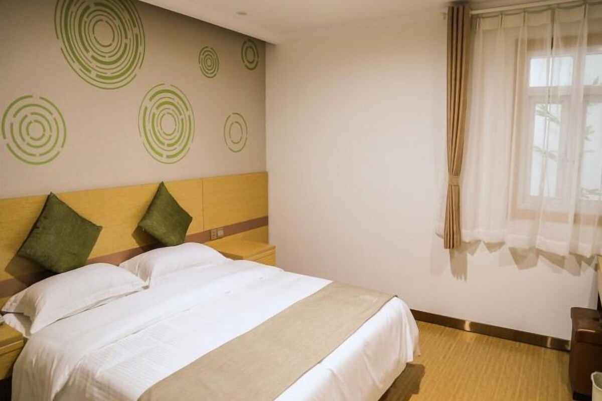 A hotel room with a bed, two pillows, a nightstand, a wall with circular patterns, and a window with curtains.