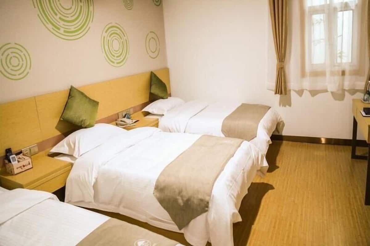 Ein Hotelzimmer mit drei Betten, einem Holzkopfteil, einem Nachttisch mit Lampe und einem Fenster mit Vorhängen.