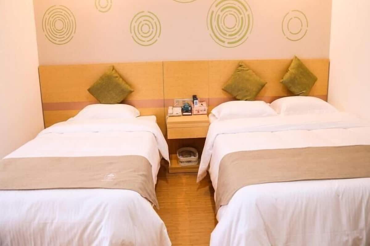 Ein Hotelzimmer mit zwei Betten, einem hölzernen Kopfteil und einem Nachttisch mit Pflegeprodukten.