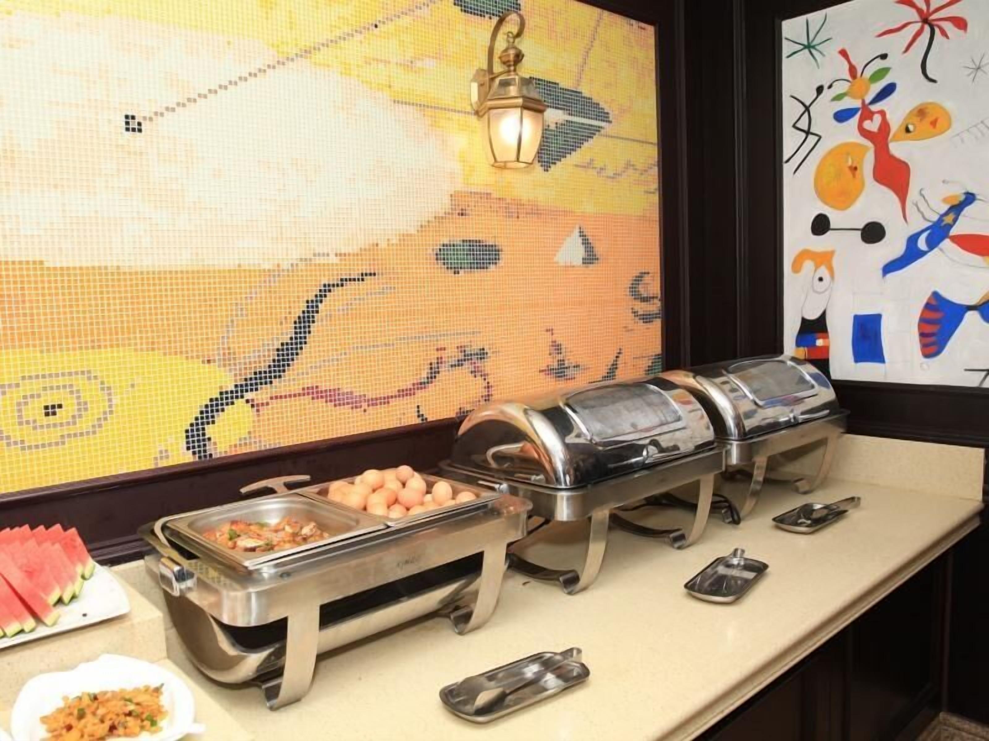 A buffet setup with various food containers and a decorative wall with abstract art.