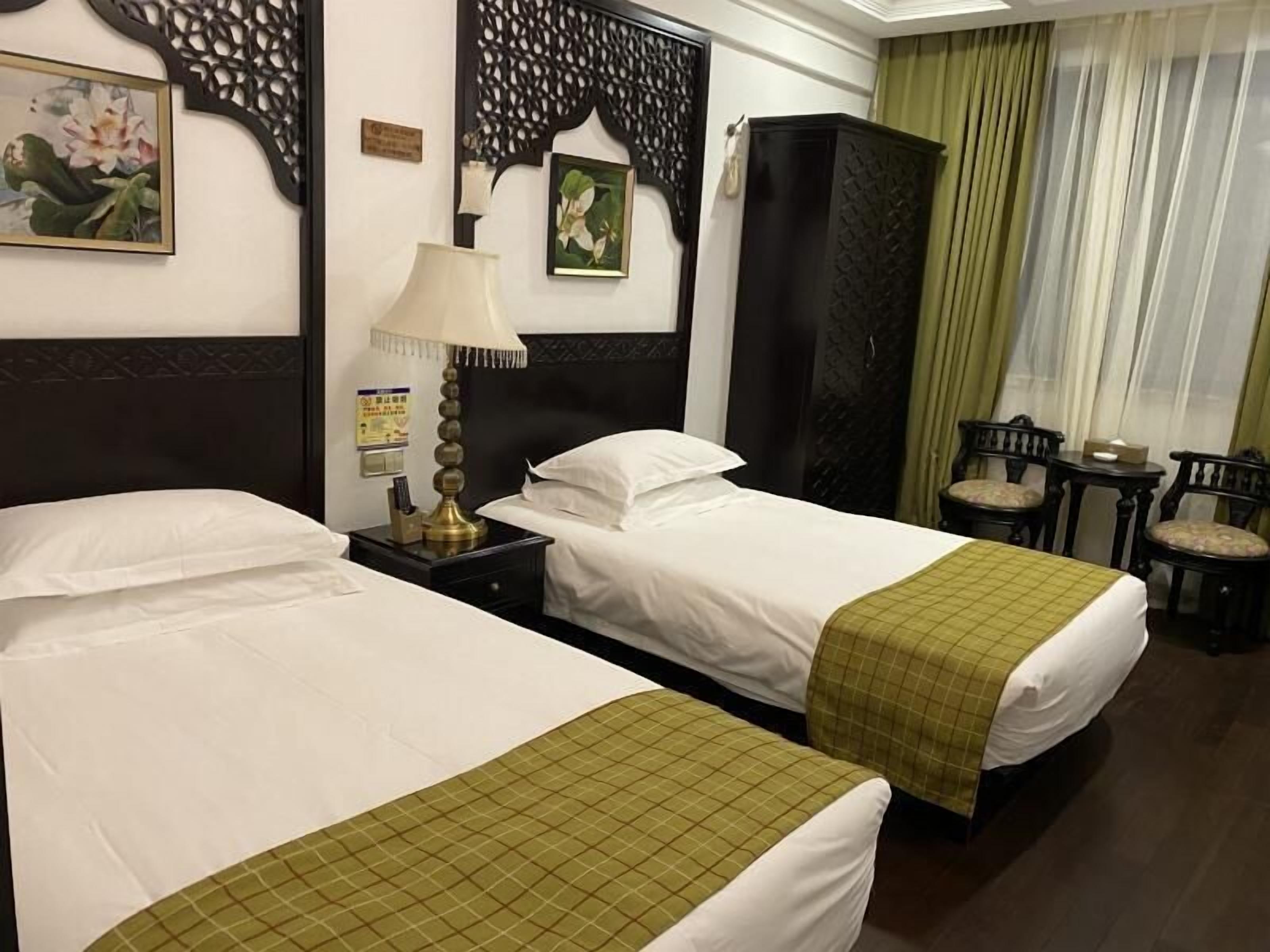 Una habitación de hotel con dos camas, una mesita de noche, una lámpara, un armario y una pequeña mesa con sillas.
