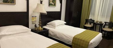Una habitación de hotel con dos camas, una mesita de noche, una lámpara, un armario y una pequeña mesa con sillas.