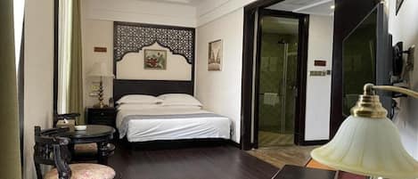 A hotel room with a bed, a desk, a chair, a lamp, and a decorative wall panel.