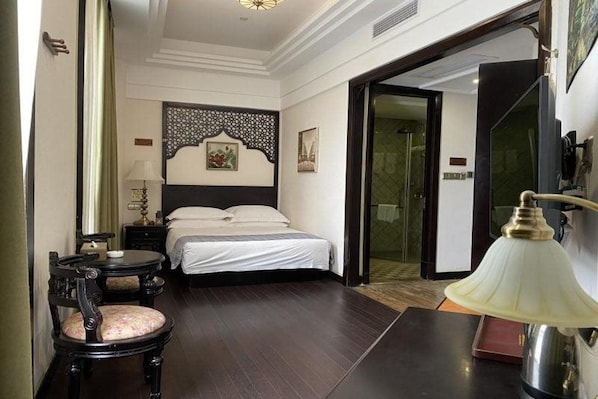 A hotel room with a bed, a desk, a chair, a lamp, and a decorative wall panel.