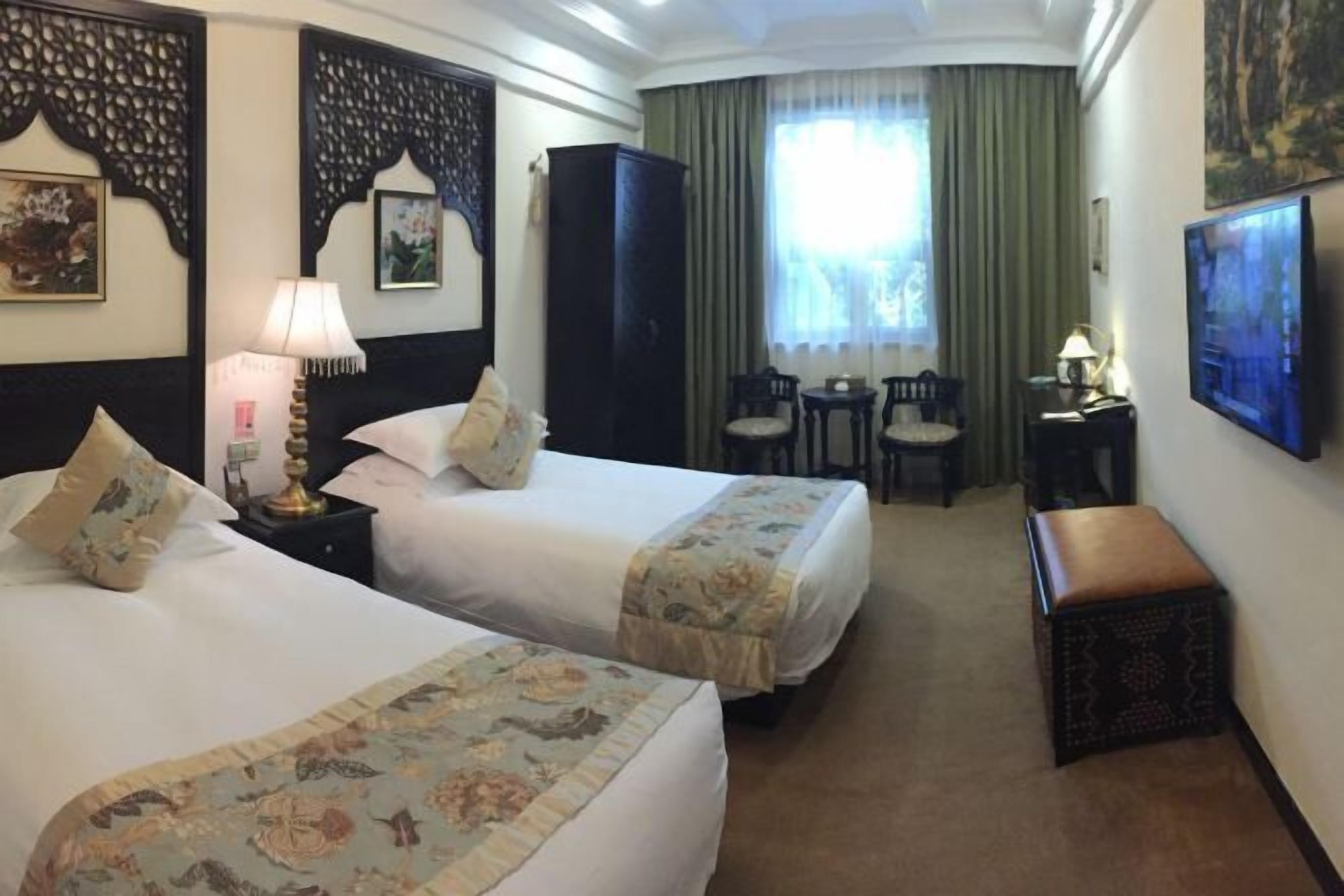 A hotel room with two beds, a desk, a chair, a small table, and a television.