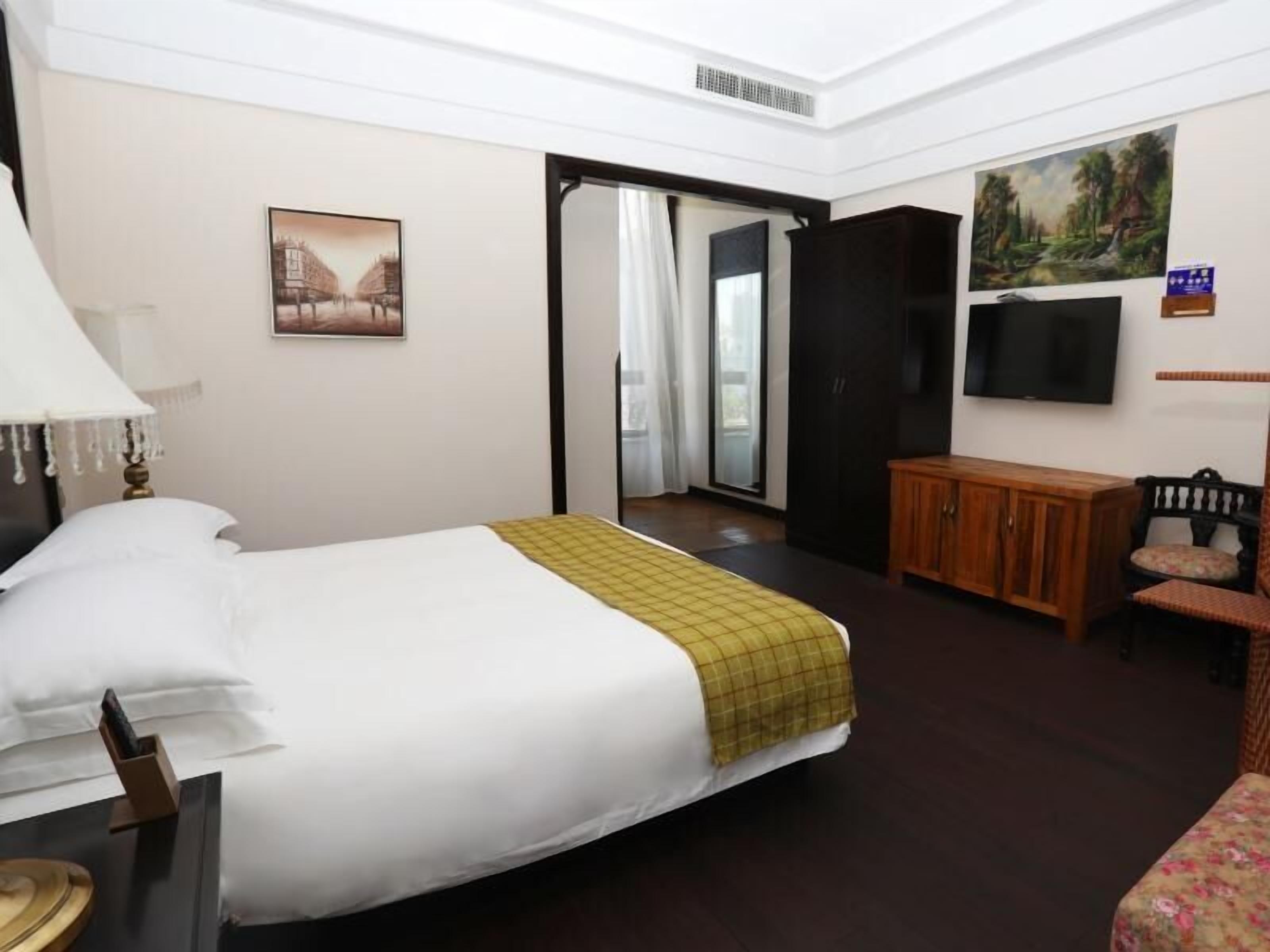 A hotel room with a bed, a desk with a lamp, a television, a cabinet, and a chair.