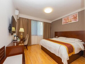 Habitación de hotel con cama, escritorio con lámpara, silla, televisión y ventana con cortinas.