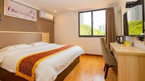 A hotel room with a bed, a desk, a chair, a window with curtains, and a view of greenery outside. - Shell Wuxi Binhu District Daoxiang New Village Hotel (Wuxi)