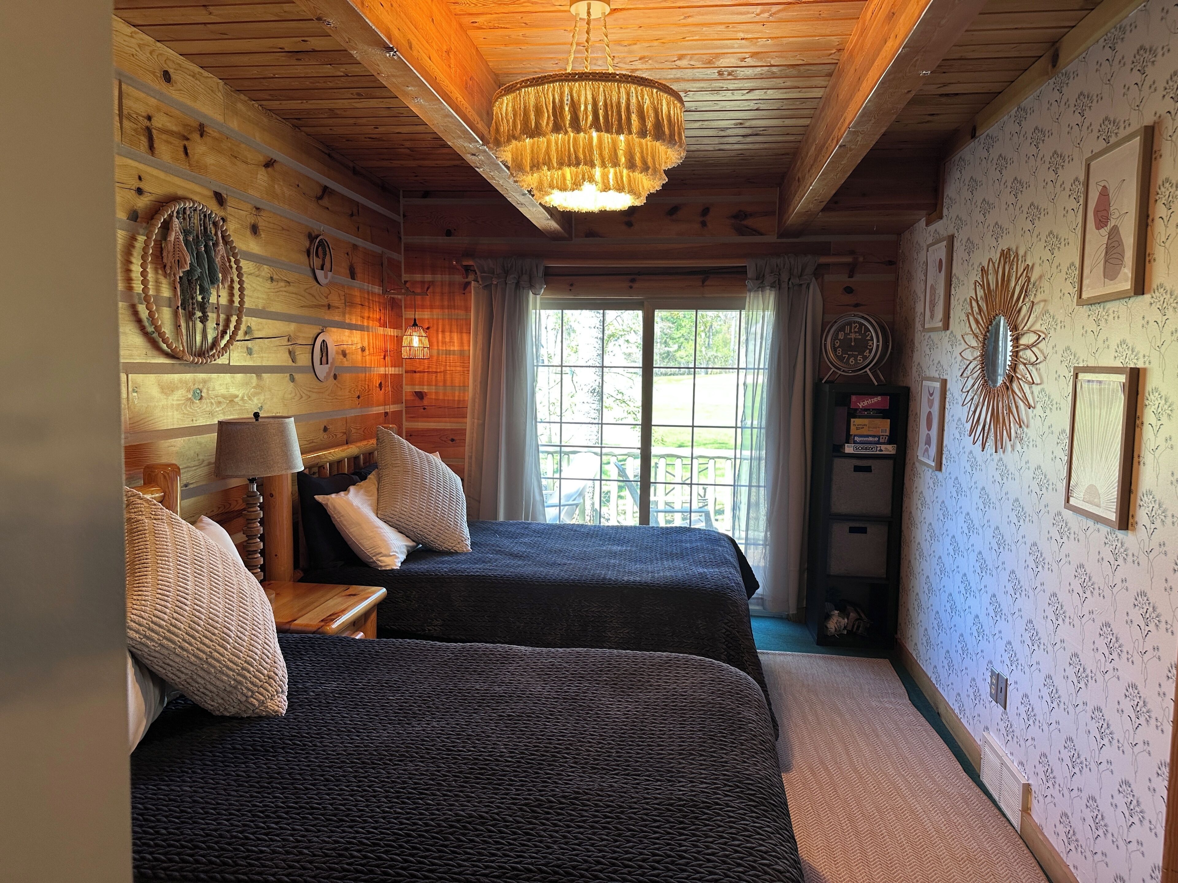 Une chambre avec deux lits, un lustre, des murs en bois et une fenêtre avec des rideaux.