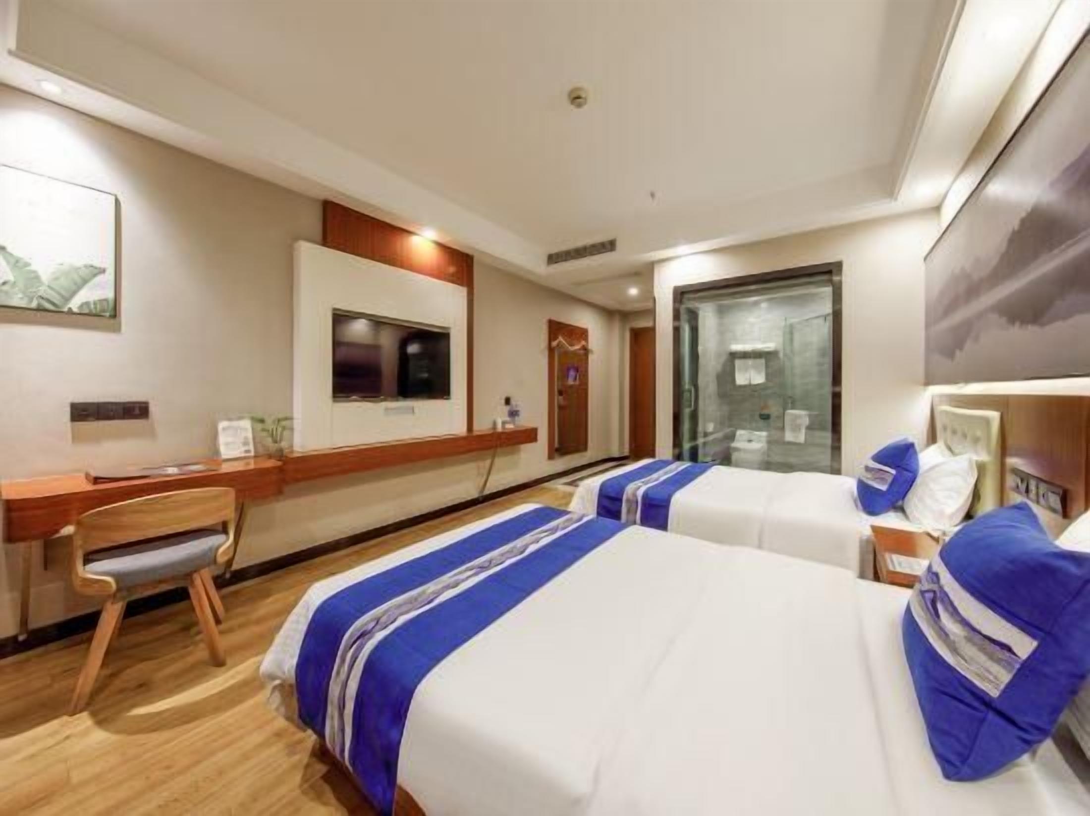 A hotel room with two beds, a desk, a chair, a TV, and a large window.