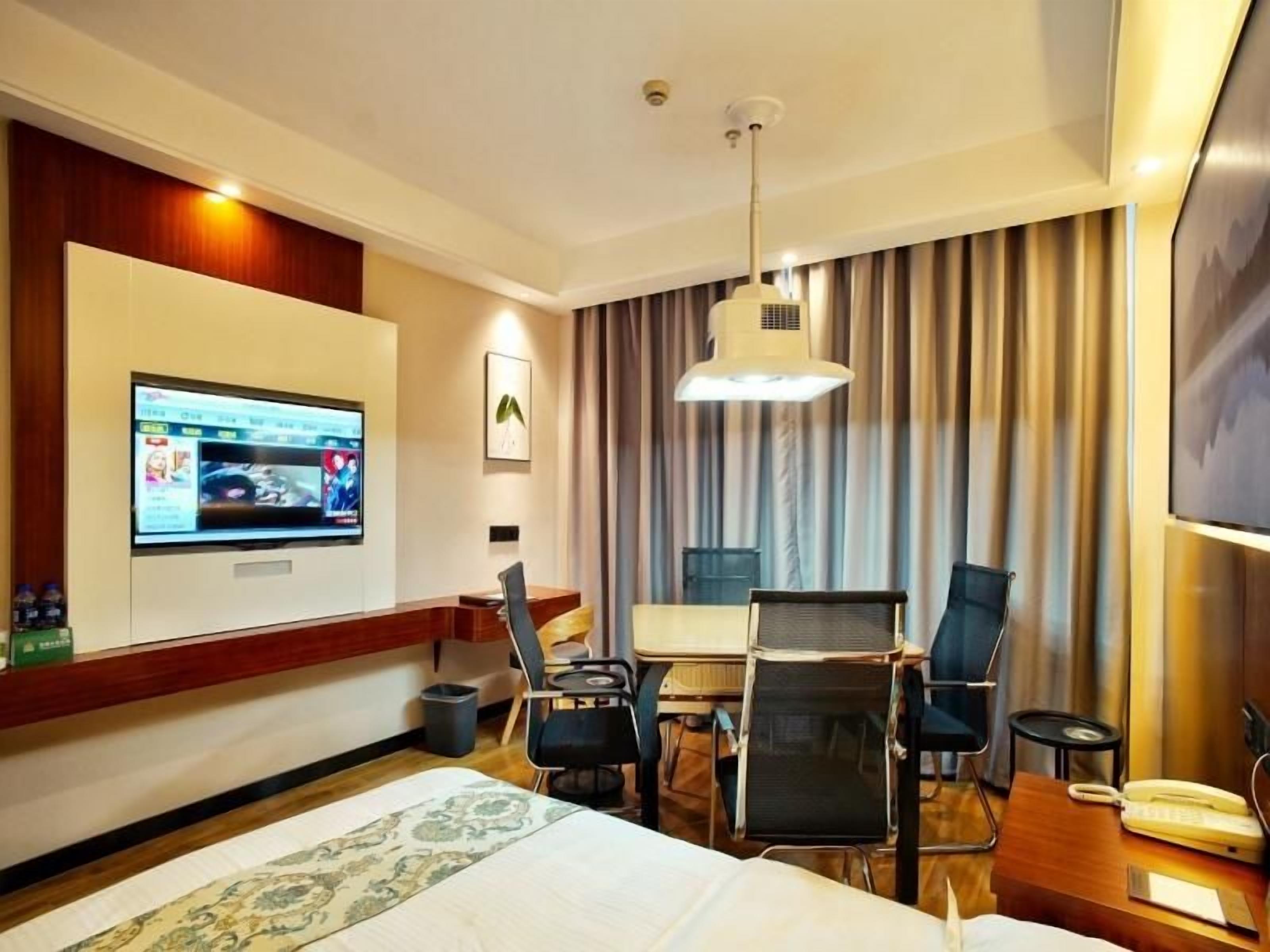 Una habitación de hotel con cama, escritorio con silla, televisor montado en la pared y cortina.