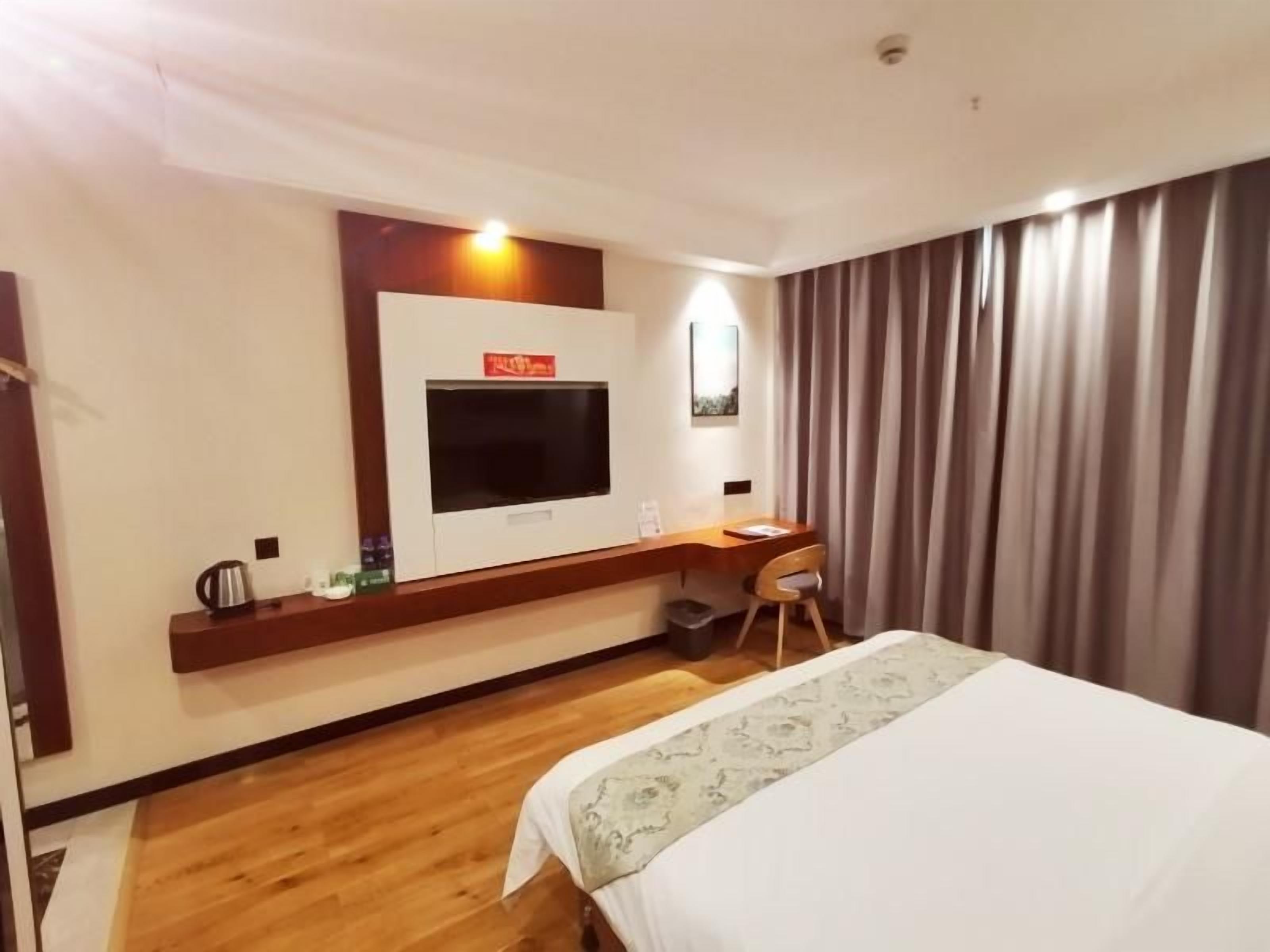 Una habitación de hotel con cama, escritorio, televisor y cortina.