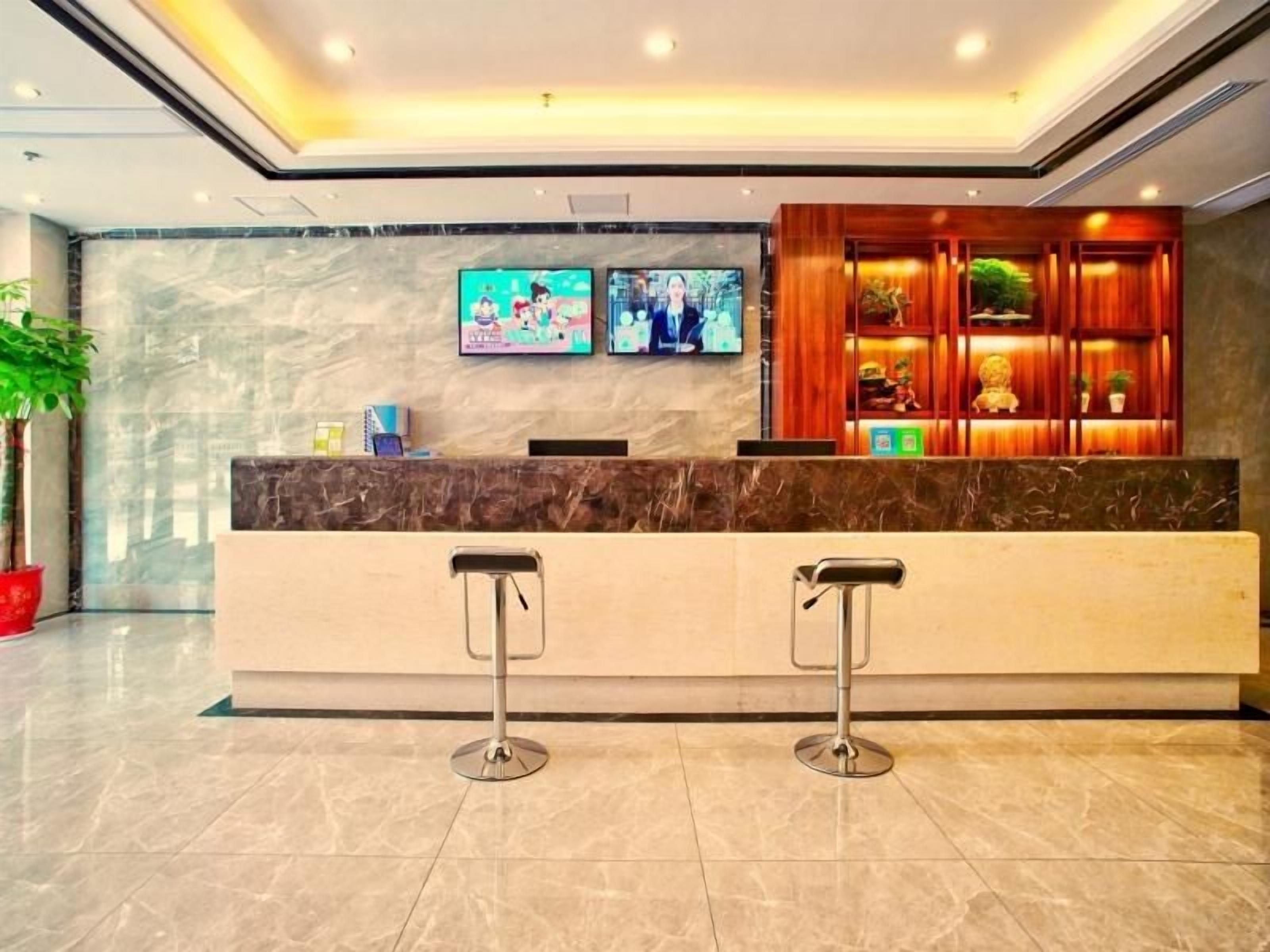 Un área de recepción con mostrador de mármol, dos taburetes de bar y dos televisores montados en la pared.
