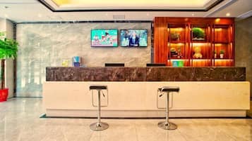 Un área de recepción con mostrador de mármol, dos taburetes de bar y dos televisores montados en la pared.