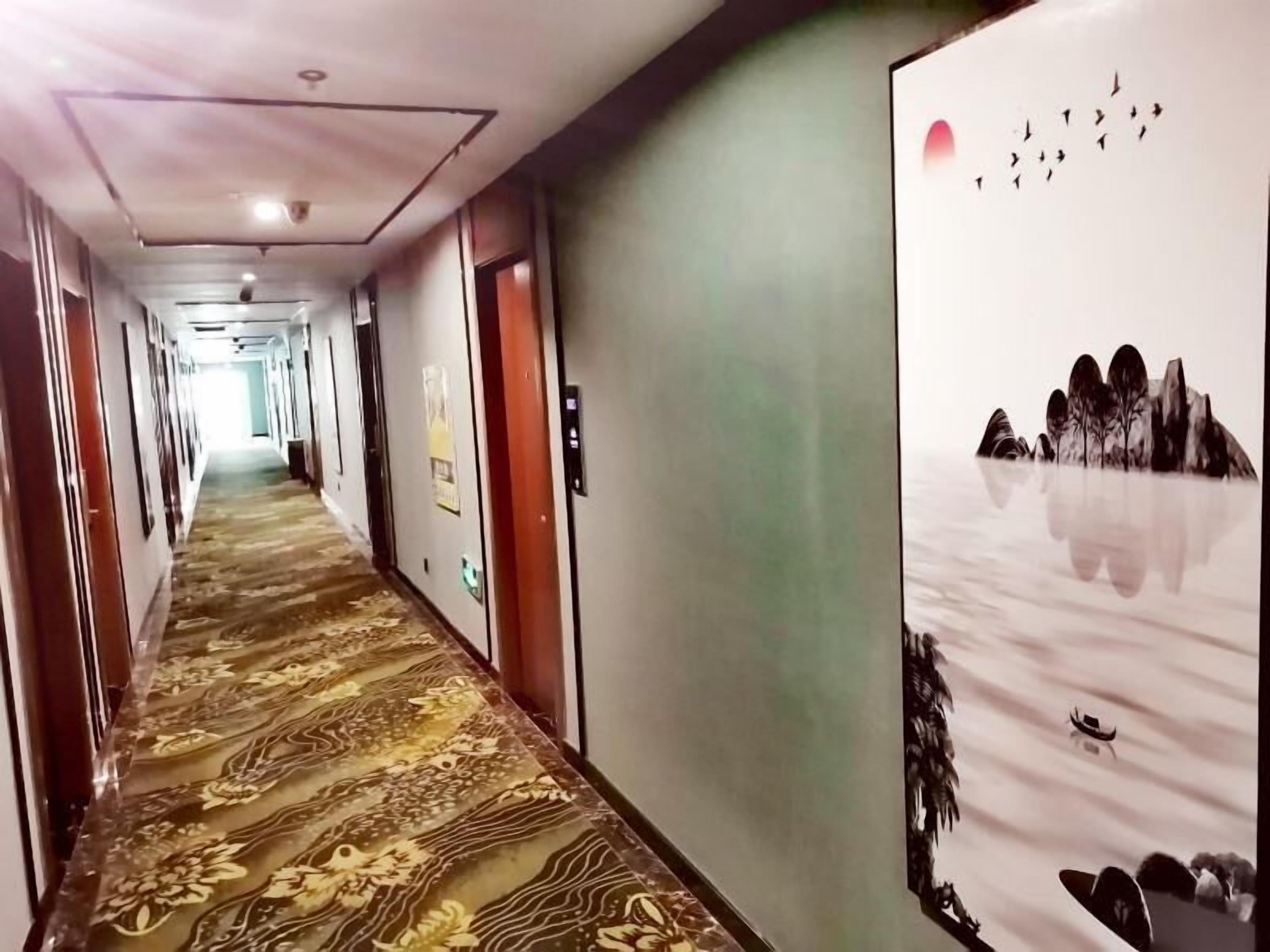 Pasillo de hotel con alfombra estampada, puertas y una pared con un mural de temática natural.