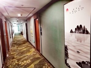 Un couloir d’hôtel avec un tapis à motifs, des portes et un mur orné d’une fresque sur le thème de la nature.