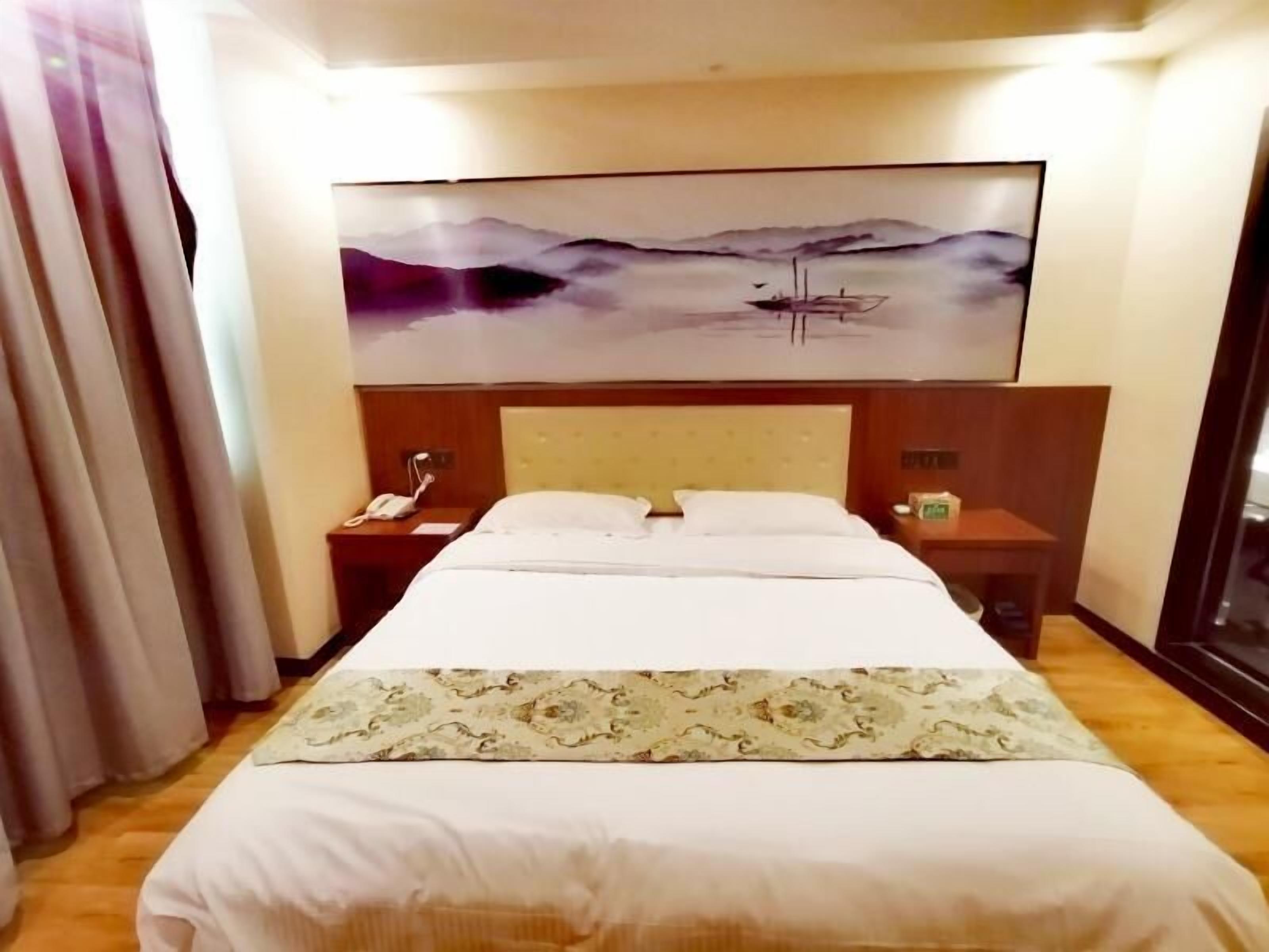 Habitación de hotel con cama, mesita de noche, teléfono y un cuadro de un paisaje en la pared.