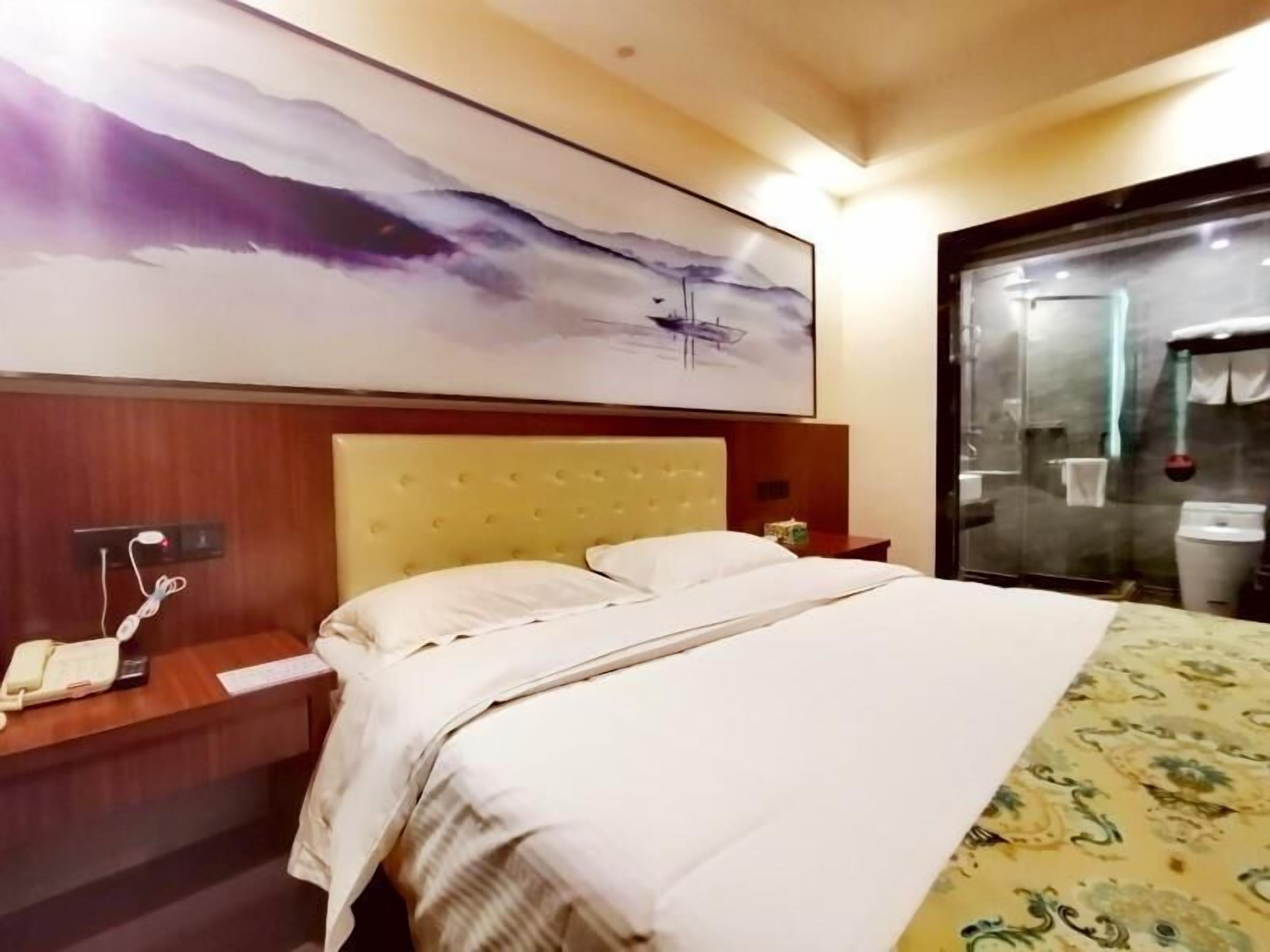 A hotel room with a large bed, a wooden headboard, a bedside table with a phone, and a painting above the bed.