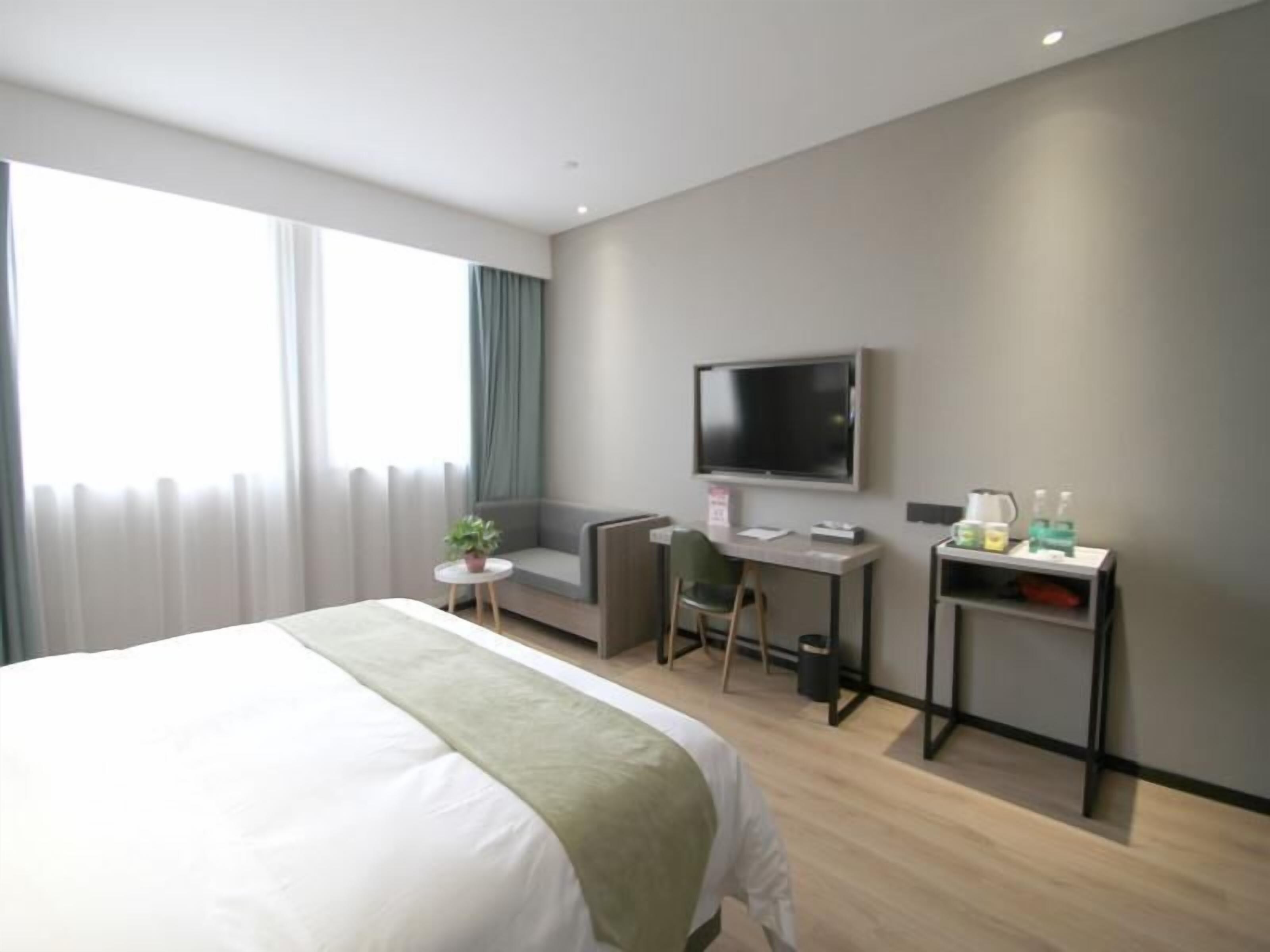 Een moderne hotelkamer met een groot bed, een bureau met stoel, een televisie en een klein tafeltje met toiletartikelen.