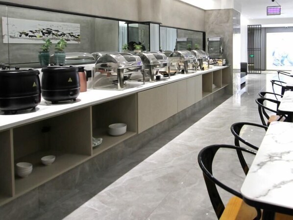 A modern buffet setup with clear food service stations, a marble-topped table, and black chairs.