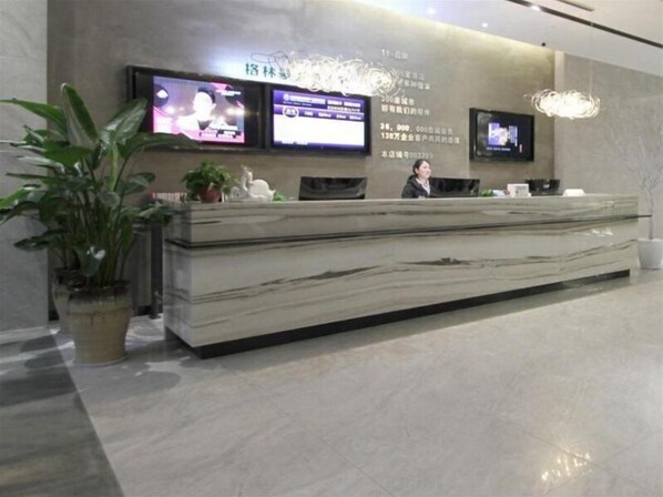 Un taulell de recepció amb dos monitors, un banc de marbre i plantes en testos.