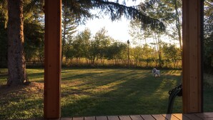 A wooden deck with a view of a grassy yard and trees. - Swan Mntn View--Entire, Private Basement Suite, Close to GNP, Whitefish & Lake. (Kalispell)