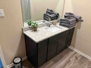 Un baño con encimera de granito, armarios oscuros, un lavabo y un espejo.