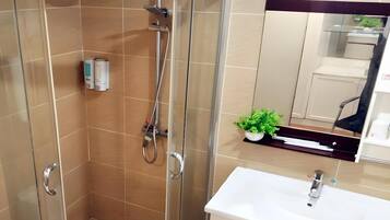 Een moderne badkamer met een douchecabine van glas, een wit wastafelmeubel en een kleine pot met een plantje.