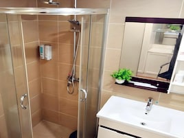 Un baño moderno con ducha de vidrio, lavamanos blanco y una pequeña planta en maceta.