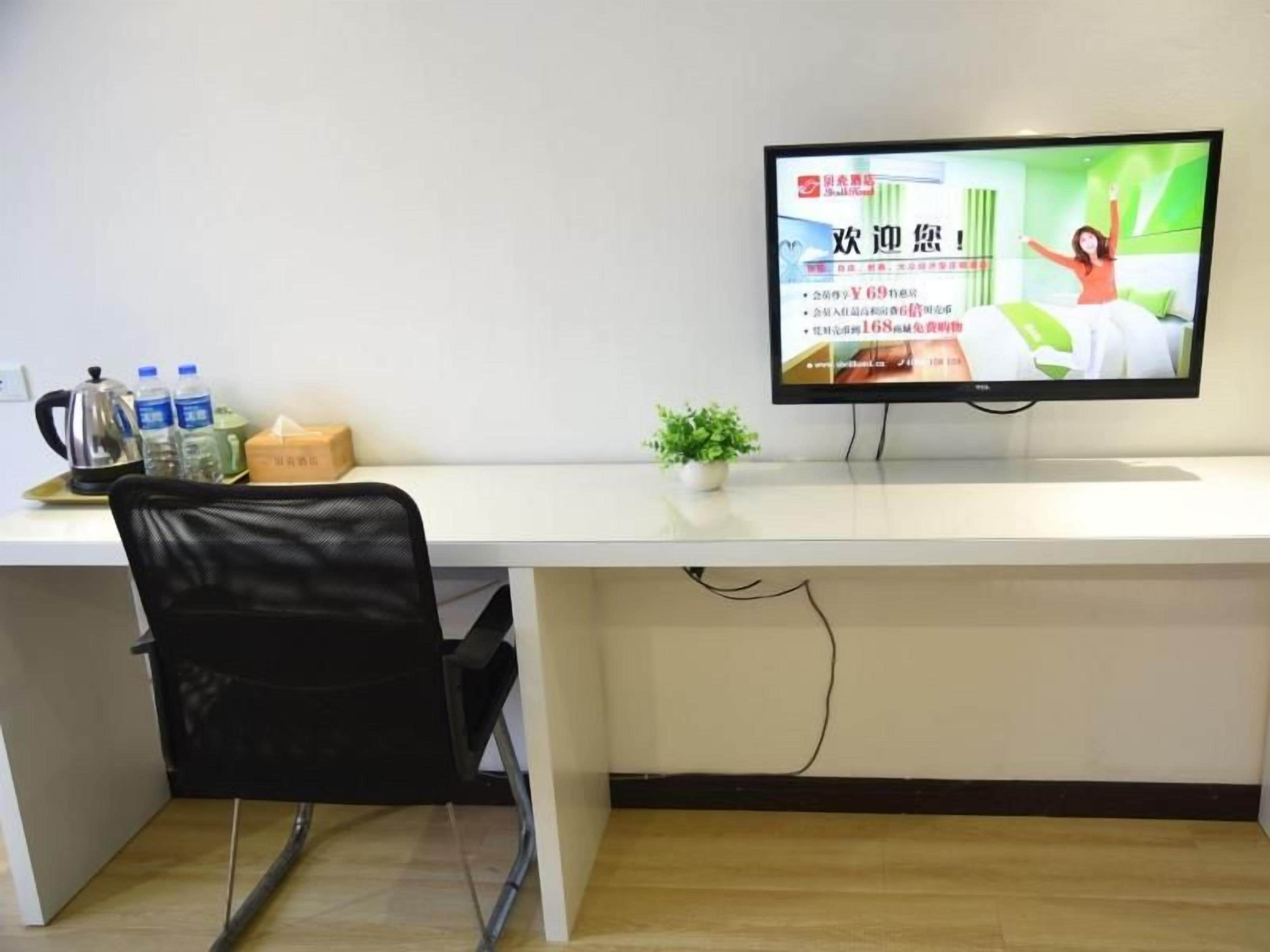Une pièce comprenant un bureau, une chaise, un téléviseur, une petite plante et un distributeur d’eau.