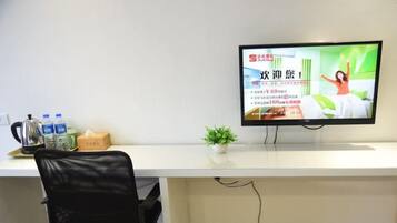 Une pièce comprenant un bureau, une chaise, un téléviseur, une petite plante et un distributeur d’eau.