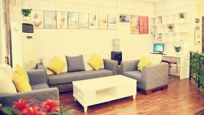 A living room with a grey sofa, white coffee table, and yellow cushions. There are framed pictures on the wall and a small plant on the side table. - Shell Lishui High-speed Railway Station Hotel (Lishui)