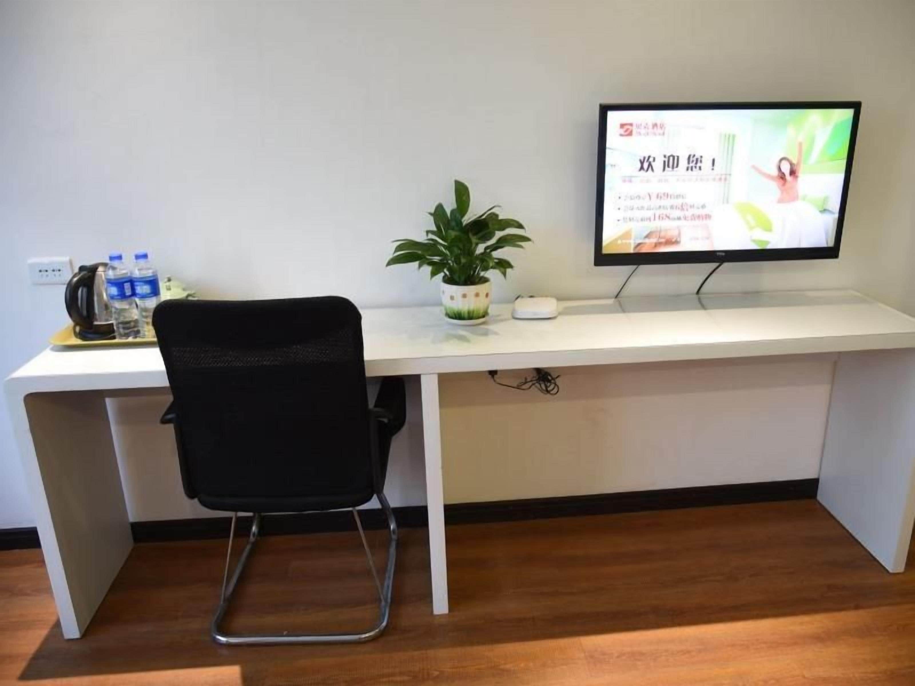 Een werkplek met een bureau, stoel, computerbeeldscherm, toetsenbord, muis en een potplant.