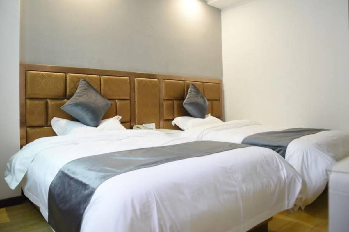 Habitación de hotel con dos camas, cabecero y mesita de noche.