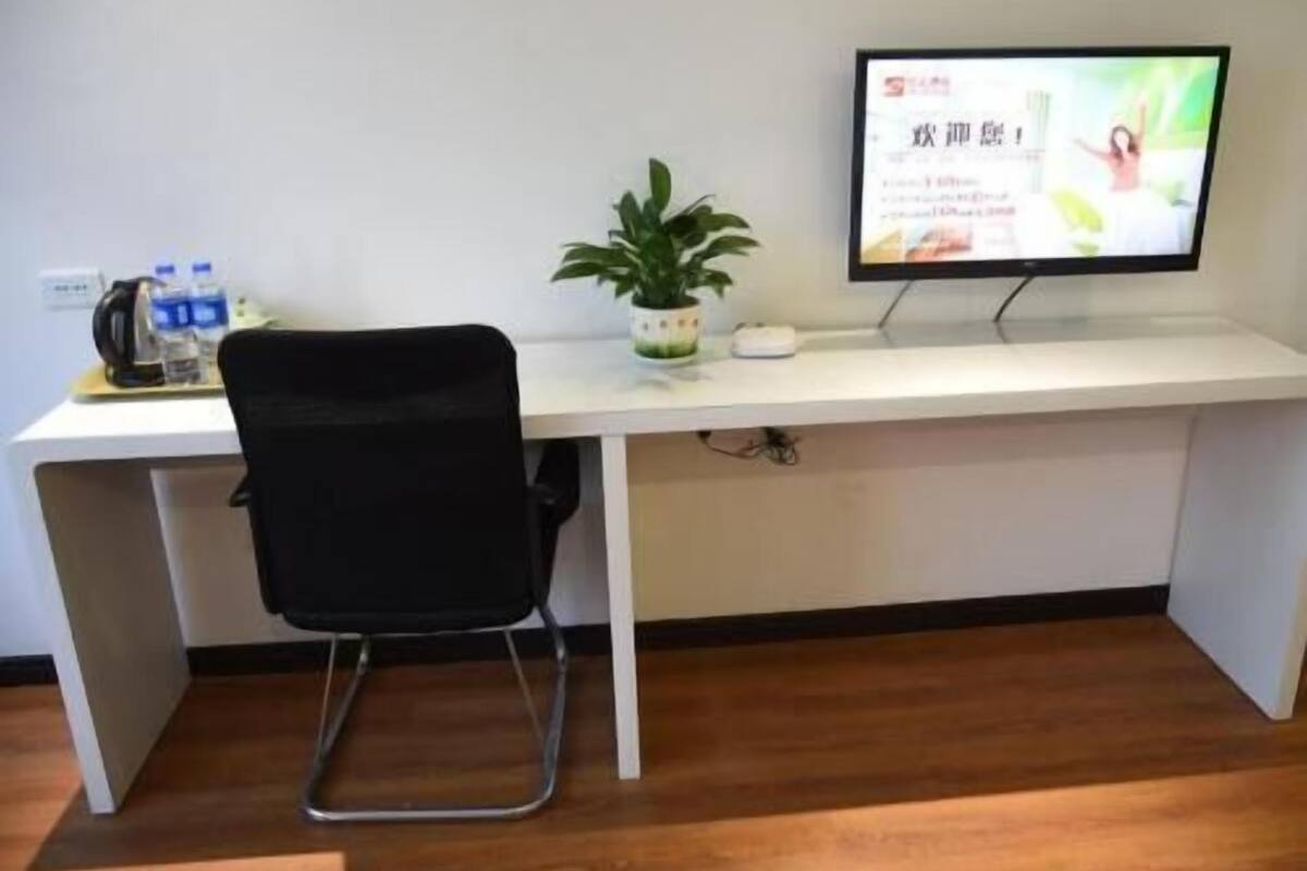 Un escritorio moderno con un monitor de computadora, una silla de oficina negra, una planta en maceta y un dispensador de agua.