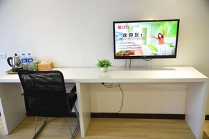 Un escritorio moderno con un televisor de pantalla plana, una silla de malla negra, una pequeña planta en maceta y una botella de agua.