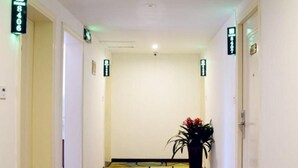 A hallway with a colorful geometric floor pattern, a potted plant, and directional signs on the walls. - Shell Lishui High-speed Railway Station Hotel (Lishui)