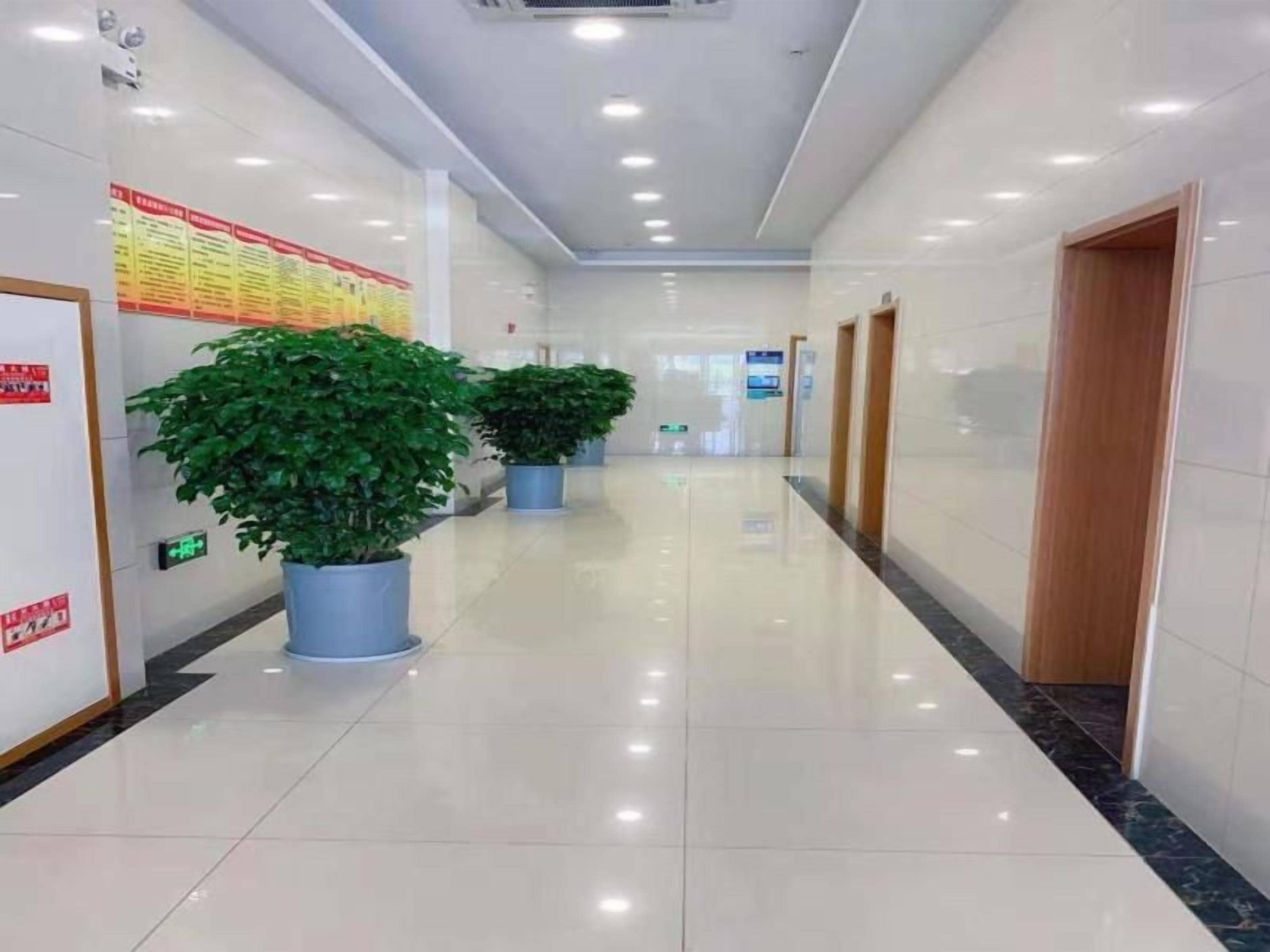 A clean, well-lit hallway with potted plants, signs, and doors.