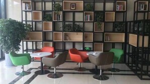 A lobby with a modern bookshelf, green and red chairs, and a tiled floor. - Greentree Inn Zhenjiang Dagang New District Tonggang Road Butterfly Square (Zhenjiang)