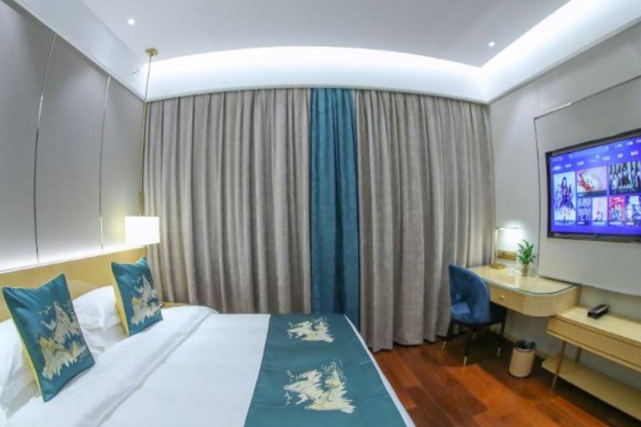 Ein Hotelzimmer mit Bett, Schreibtisch, Stuhl, Fernseher und Vorhang.