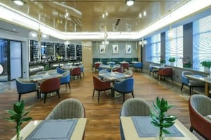 Ein geräumiges Restaurant mit mehreren Tischen und Stühlen, einer Bar und großen Fenstern mit Jalousien.