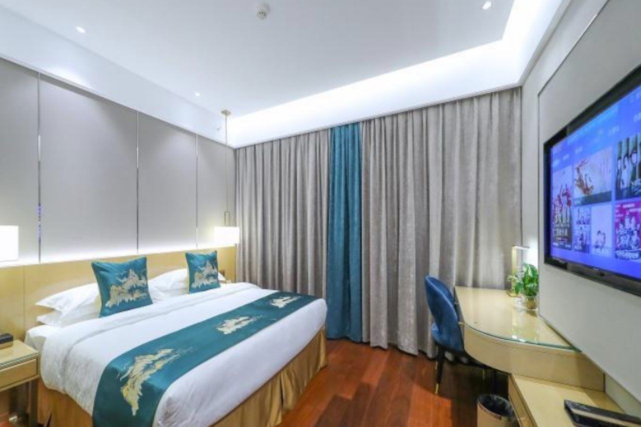 Una habitación de hotel con cama, escritorio, televisor y cortinas.
