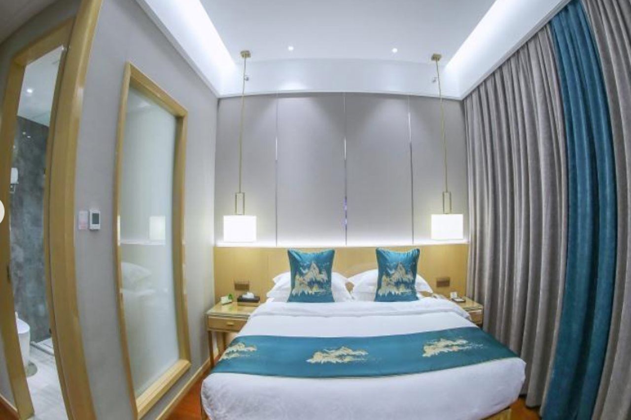Une chambre d’hôtel avec un grand lit, deux tables de chevet, un miroir et une fenêtre avec des rideaux.