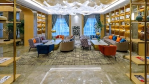A spacious lounge area with multiple seating options, a central coffee table, and a large bookshelf filled with books. - GYA Jiangsu Provinceyancheng City Oubao Liya Life Plaza Hotel (Yancheng)
