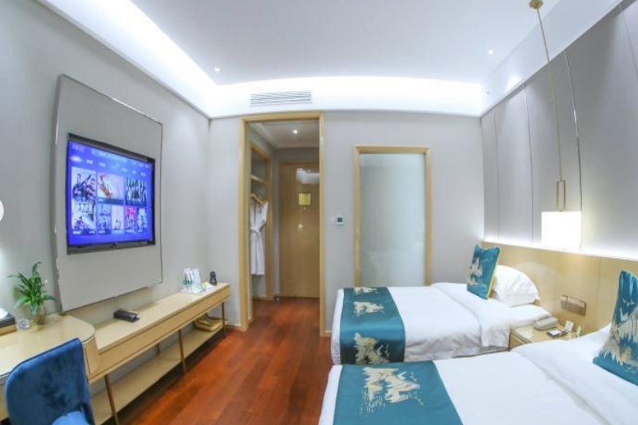 A hotel room with a bed, bedside table, TV, desk, chair, and a mirror.