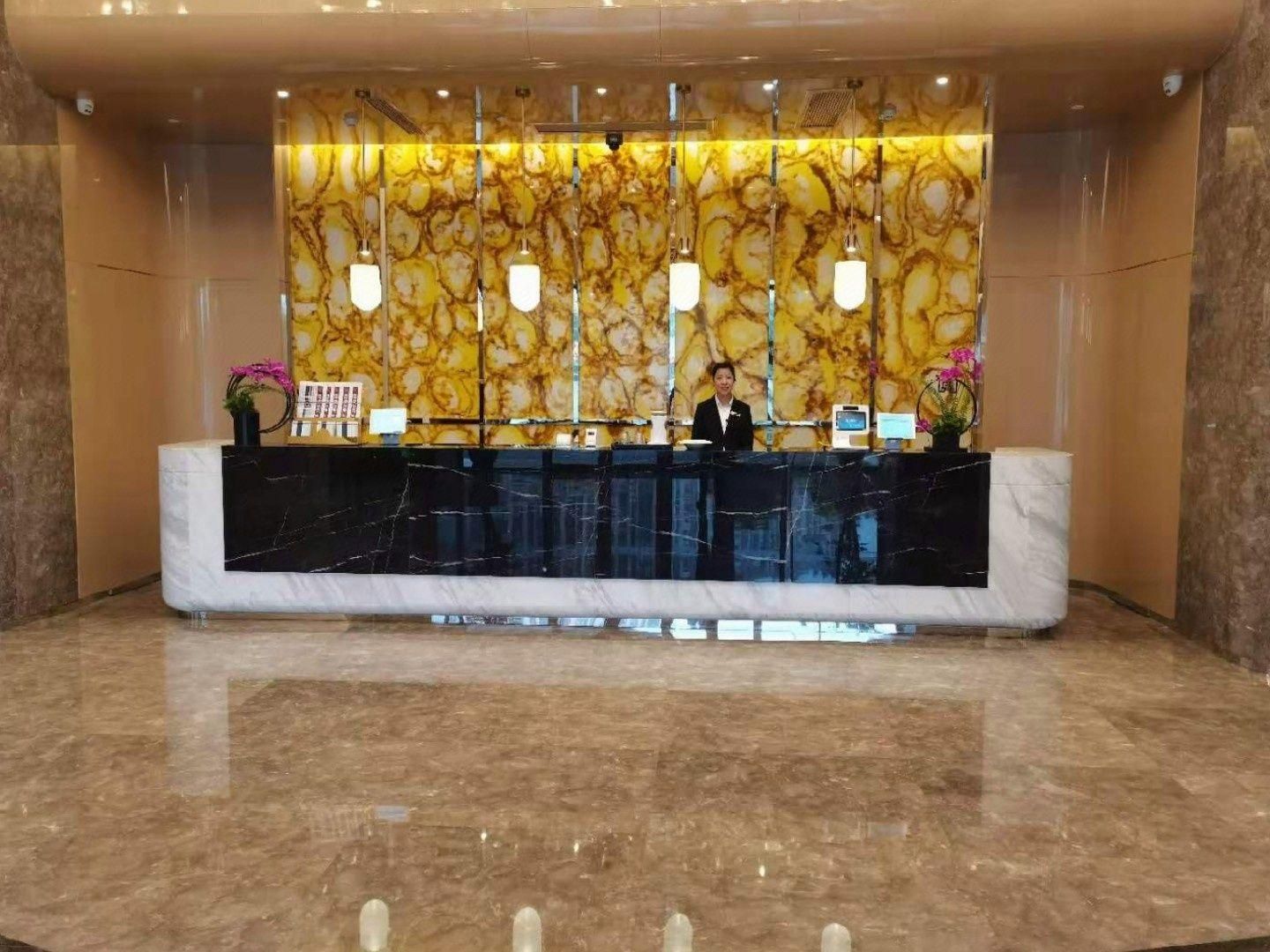 A reception desk with a marble counter, a receptionist, and a wall with a marble pattern.