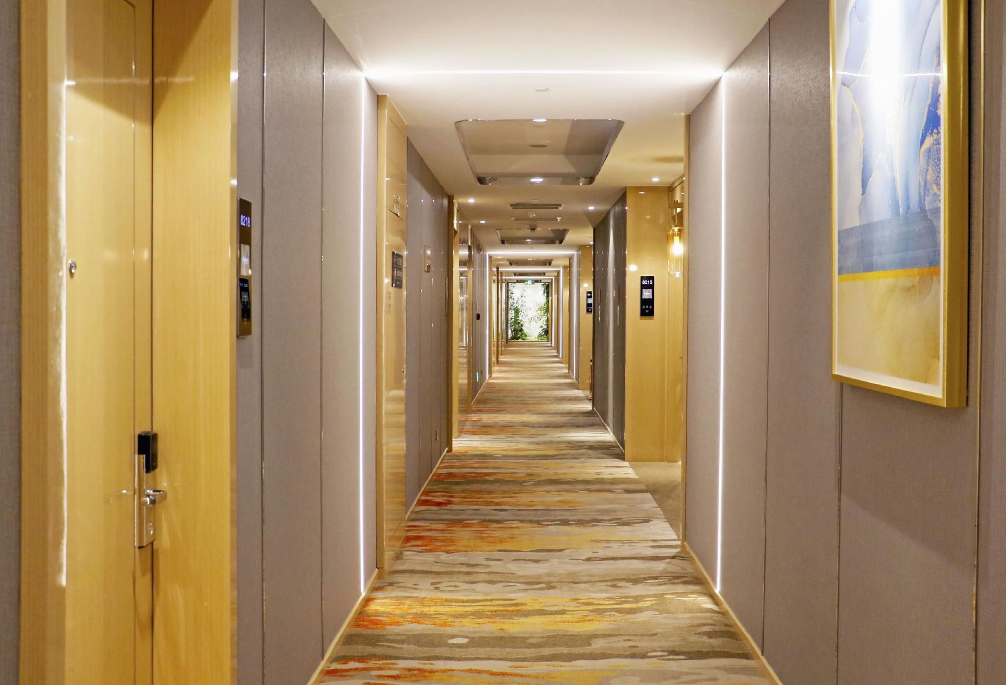 A hotel hallway with doors on both sides, a patterned carpet, and a framed picture on the right wall.