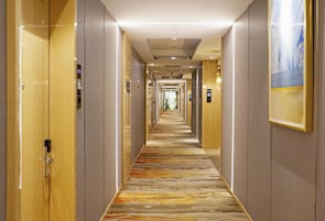 A hotel hallway with doors on both sides, a patterned carpet, and a framed picture on the right wall.