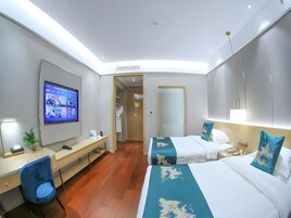 A hotel room with a desk, two beds, a TV, and a mirror.